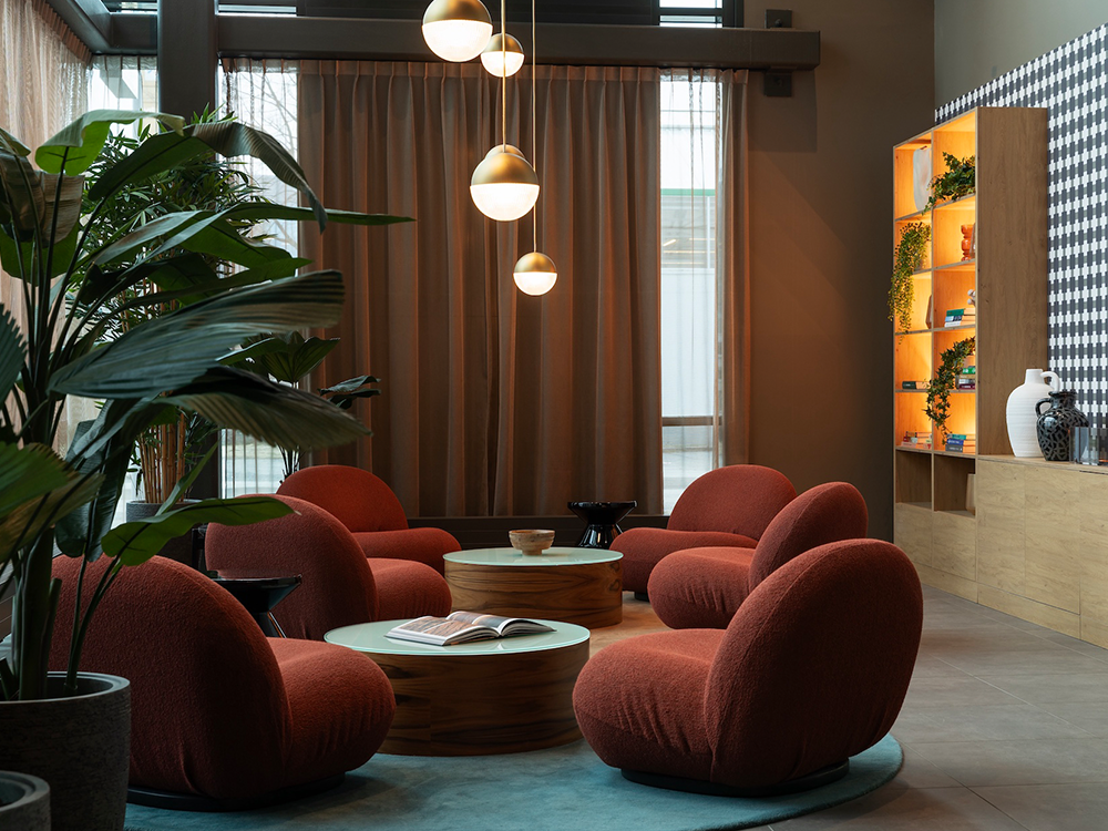Modern lounge with rust armchairs, round coffee tables, lush plants, and Massimo Copenhagen rug