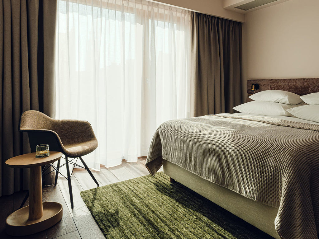 Modern hotel room with green Massimo Copenhagen rug, cozy chair, and natural light