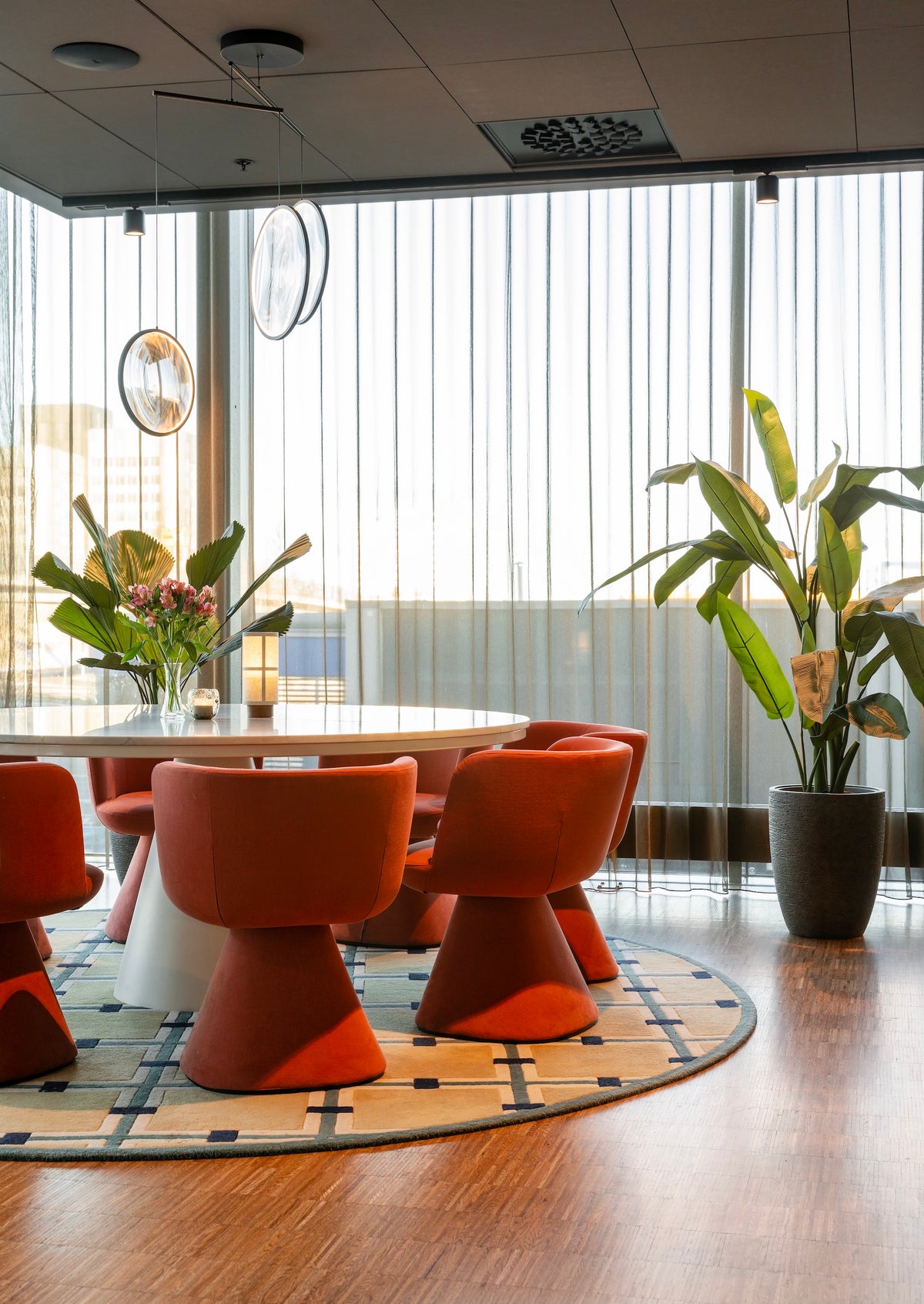 Modern dining area with orange chairs, a round table, and plants in a well-lit room.