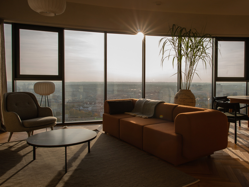 Modern living room with large windows, brown sofa, green rug, and city view, Massimo Copenhagen style