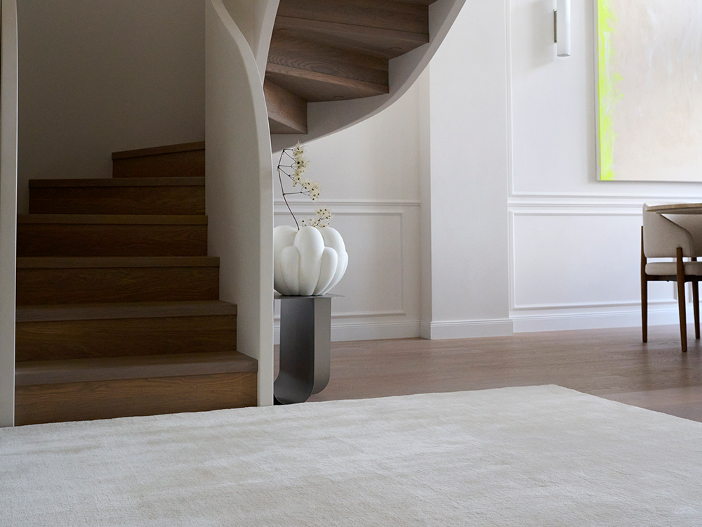 Minimalist living space with light handmade rug by Massimo Copenhagen, wooden stairs, sculptural vase, and modern art.